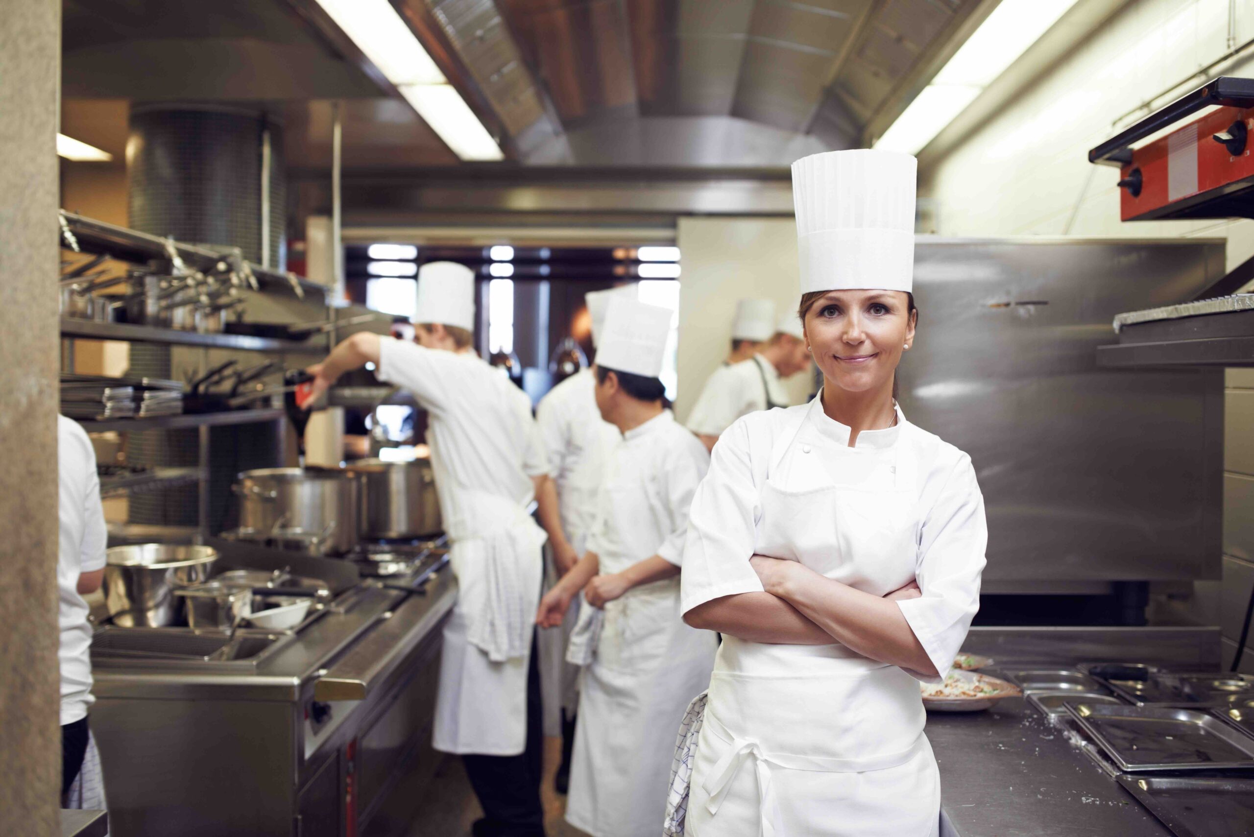 Image of woman with arms crossed for culinary service job standing in a commercial kitchen. Face of cook in food industry for catering, career and hospitality